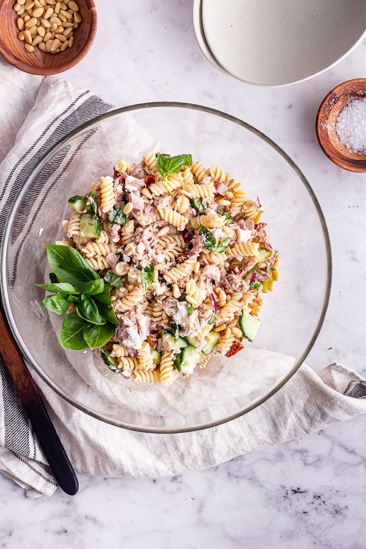 Overhead shot of tuna pasta salad in a glass bowl with salt and pine nuts