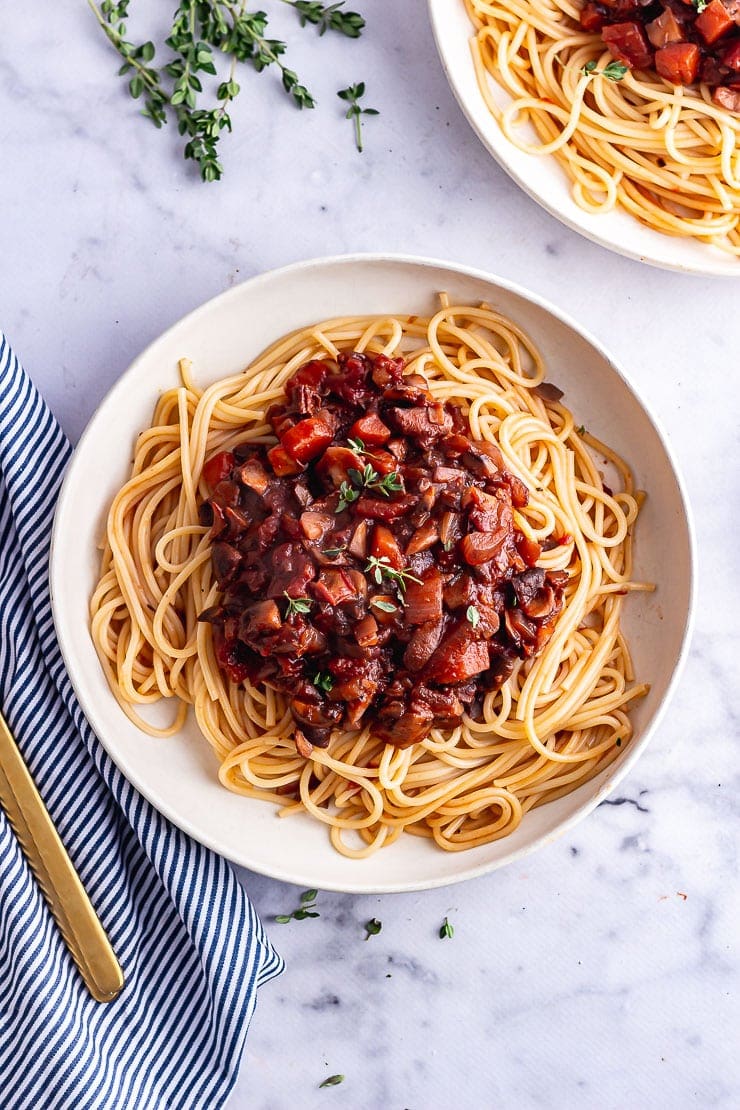 Overhead shot of vegetarian spaghetti bolognese in a white bowl on a marble surface