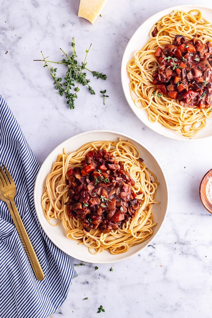 Overhead shot of two bowls of vegetarian spaghetti bolognese on a marble surface