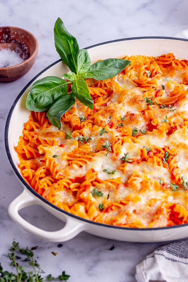 White pan of cheesy pasta with red pepper sauce on a marble surface