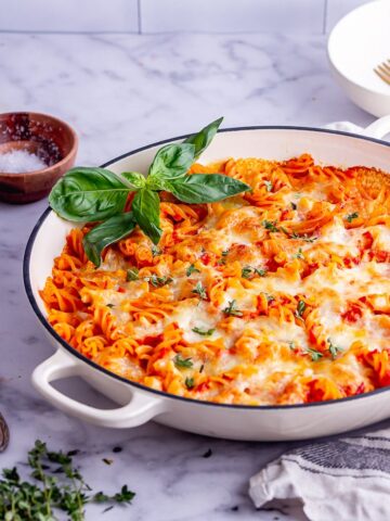 White dish of cheesy pasta bake with red pepper sauce on a marble background