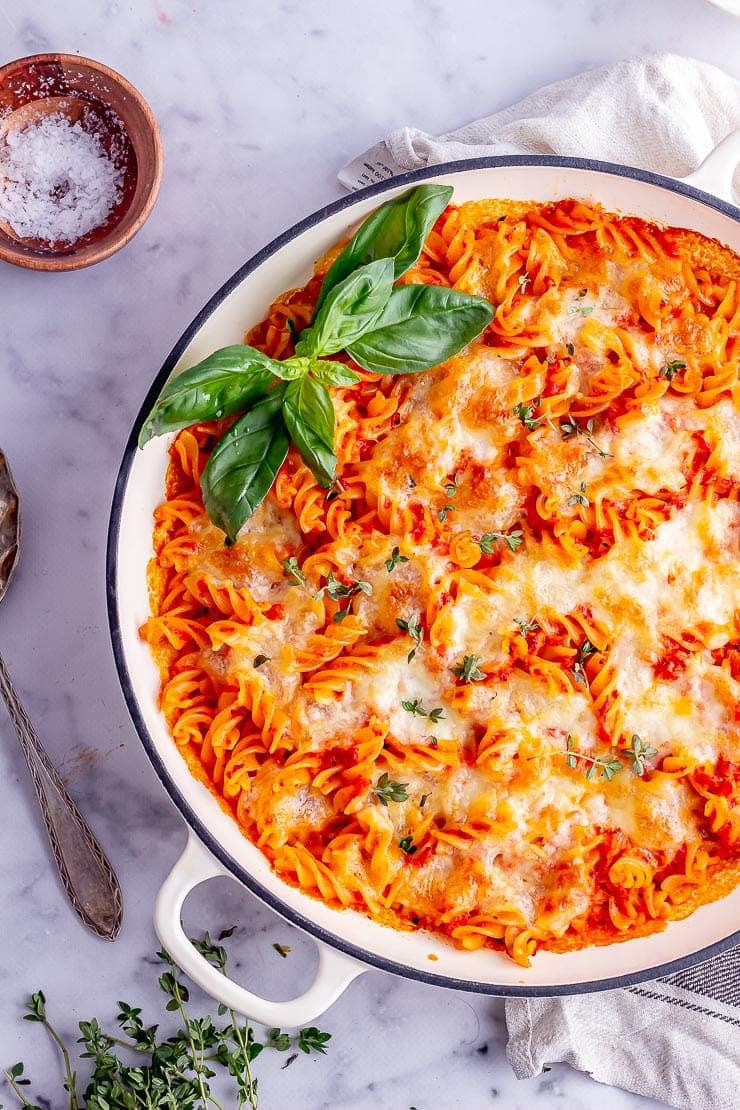 Overhead shot of red pepper pasta bake with basil leaves on a marble background