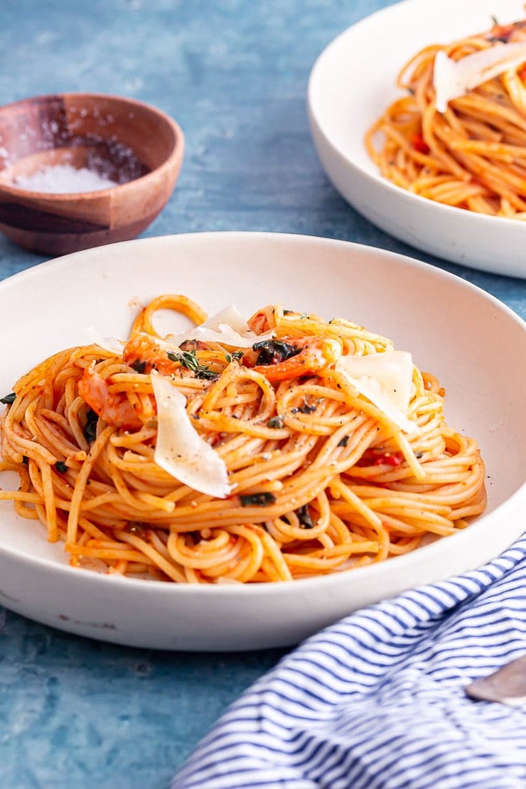 Side on shot of prawn pasta in a white bowl with a striped cloth