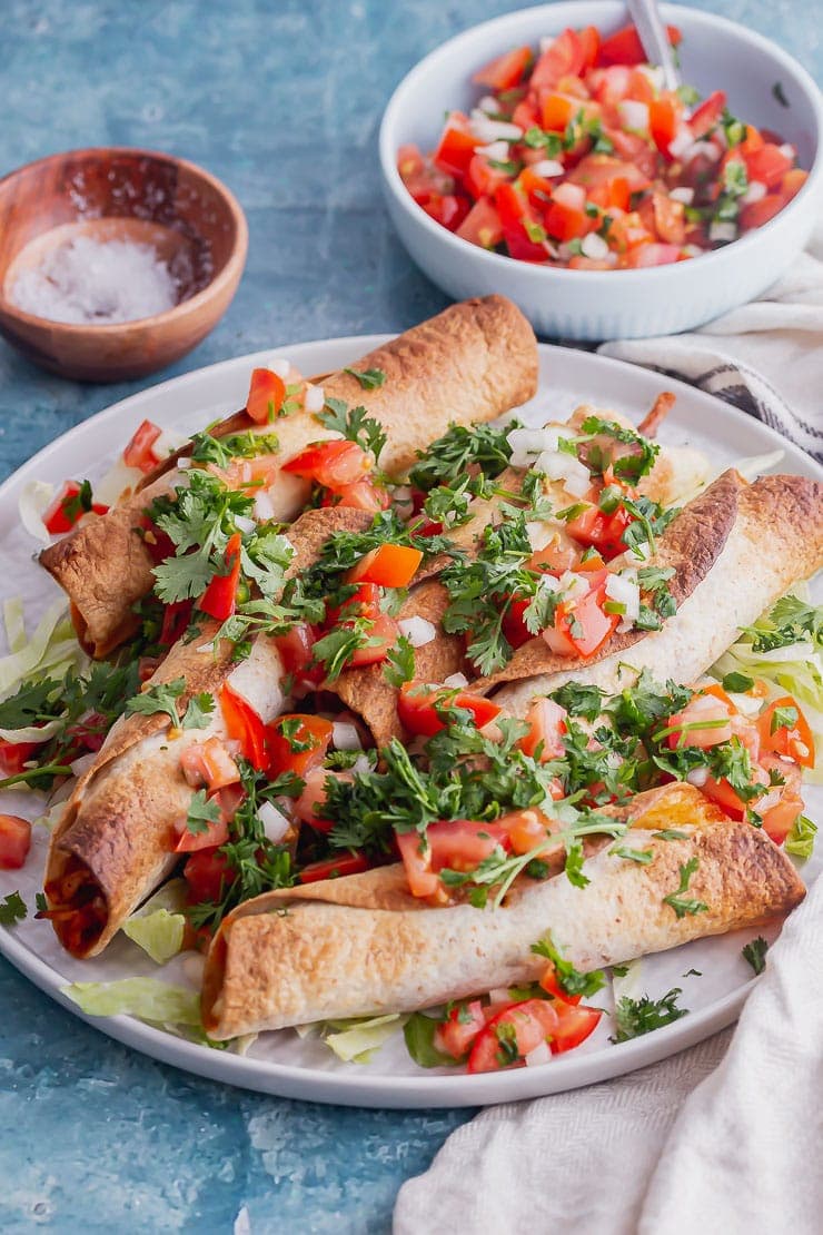 Side on shot of grey plate of taquitos with chicken and pico de gallo