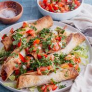 Grey plate of chicken taquitos with salsa on a blue background