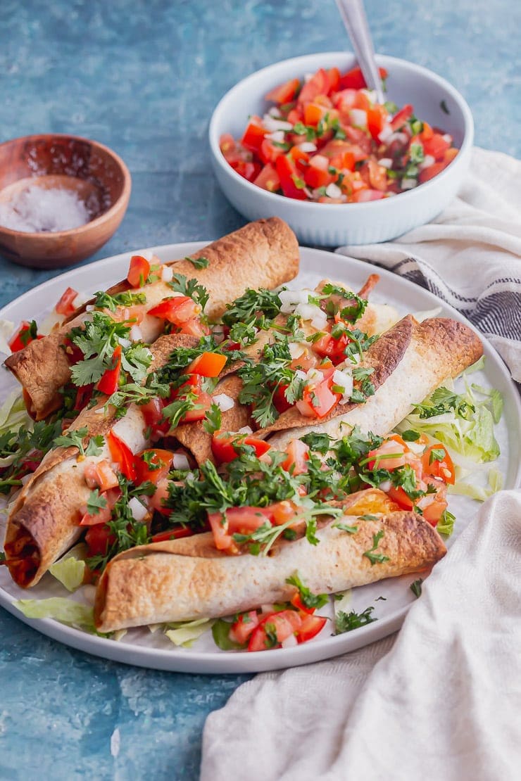 Grey plate of chicken taquitos with salsa on a blue background