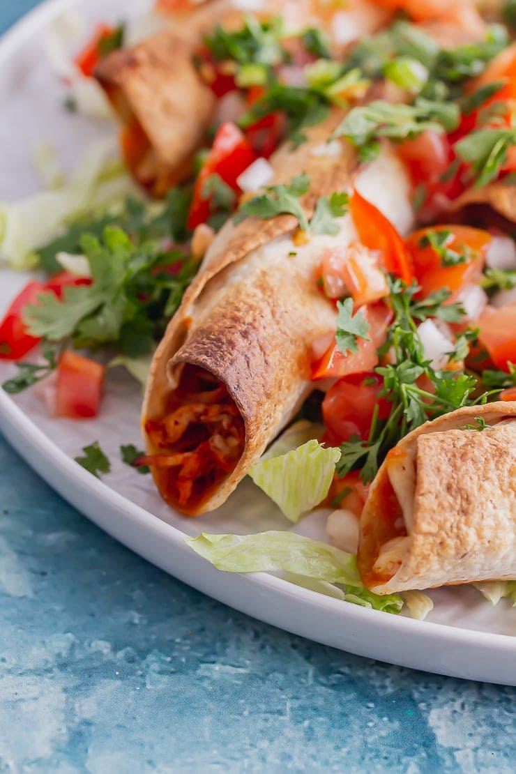 Close up of chicken taquitos with lettuce and tomato on a blue background