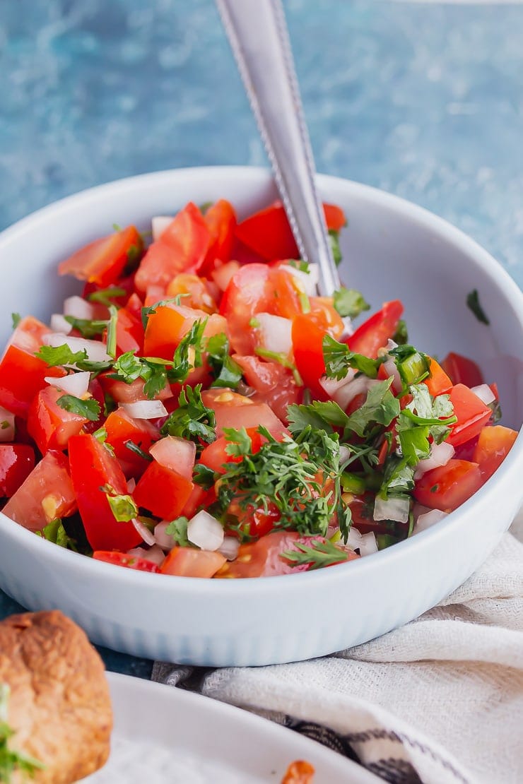 Close up of pico de gallo in a blue bowl with a spoon