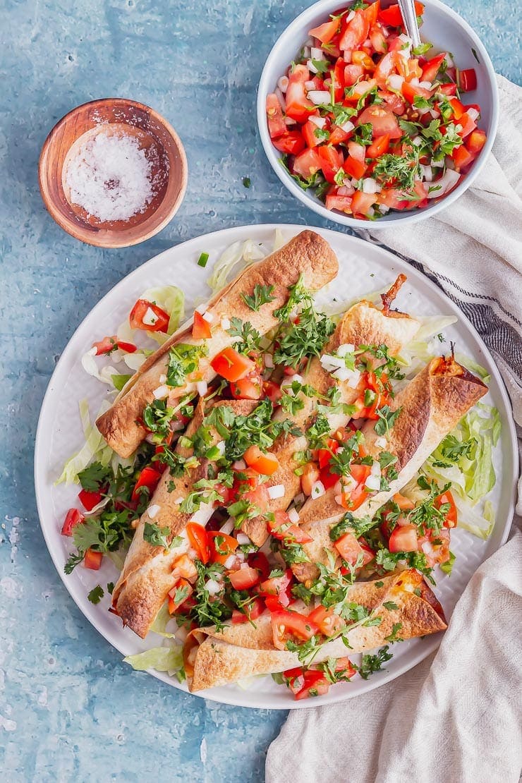 Overhead shot of taquitos on a grey plate over a blue surface