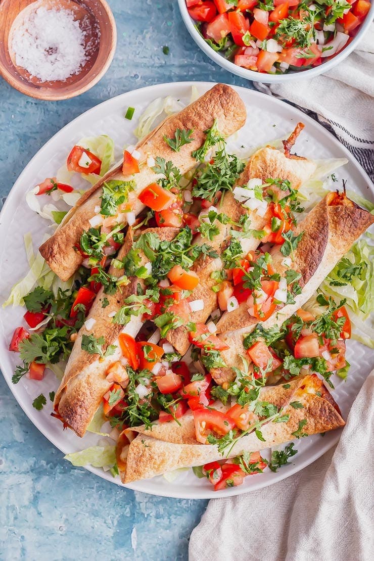 Overhead shot of taquitos on a grey plate on a blue surface