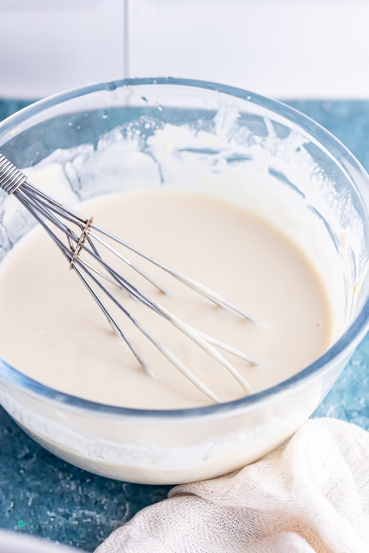 Close up of creamy tahini dressing in a glass bowl with a whisk