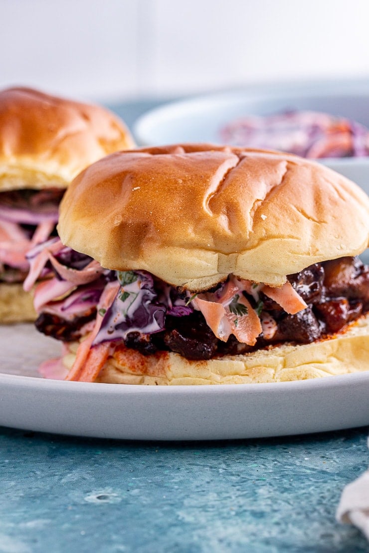 Close up of a vegan pulled pork sandwich in a brioche bun on a blue background