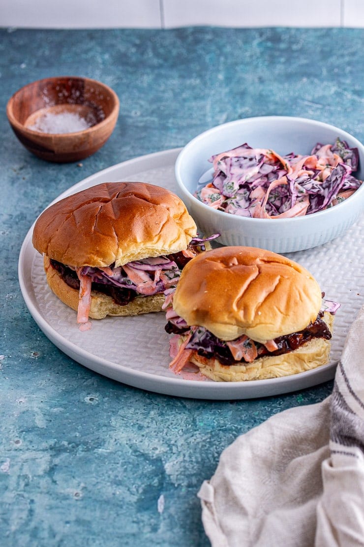Grey plate of pulled mushroom sandwiches with a blue bowl of slaw