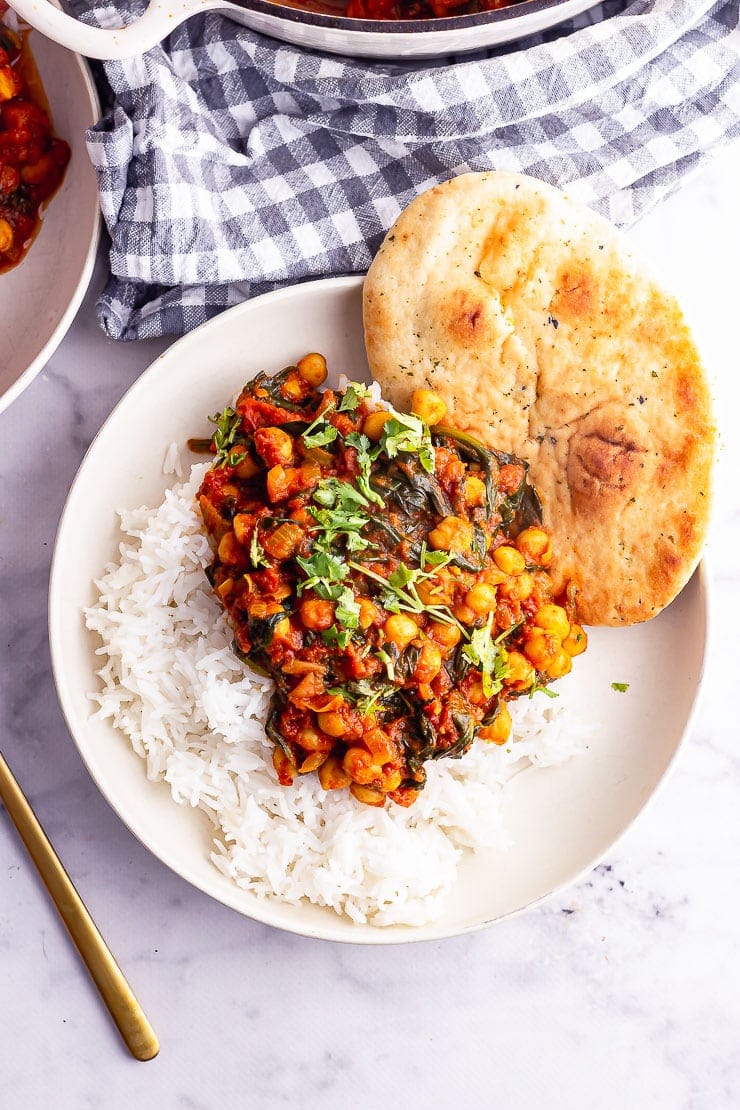 Overhead shot of spinach and chickpea curry with rice and naan in a white bowl