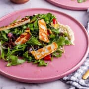 pink plate of roast vegetable salad with halloumi on a marble background