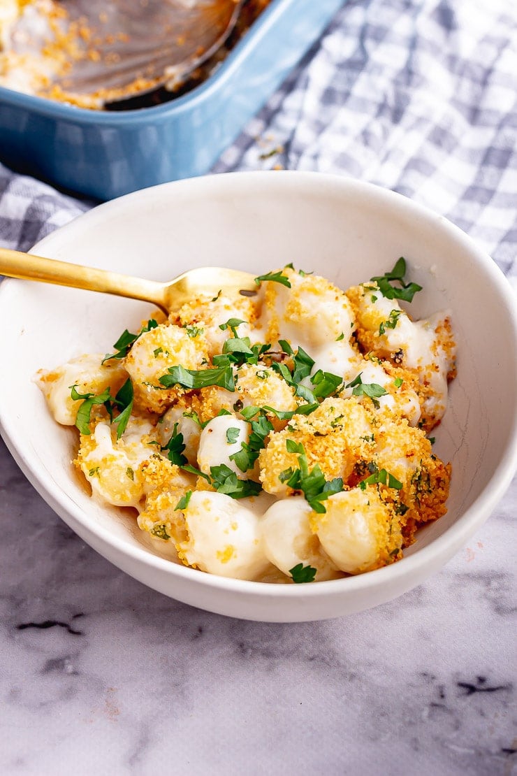White bowl of baked gnocchi with parsley and a gold fork