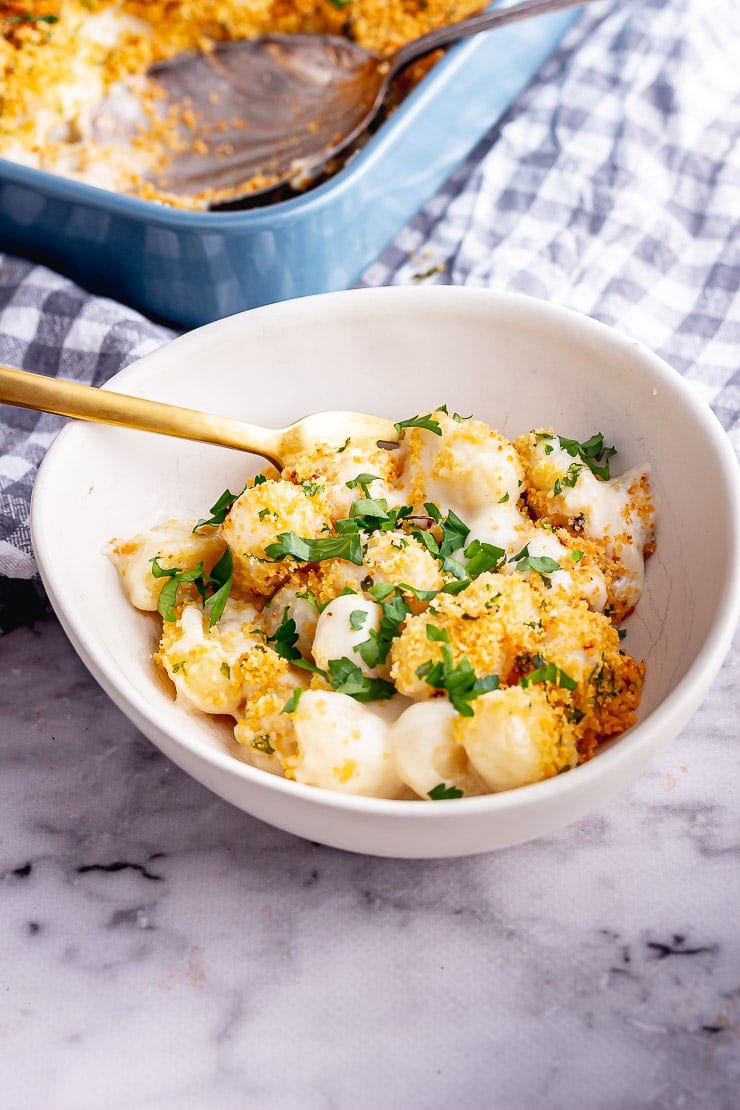 White bowl of gnocchi with cheese with a gold fork 