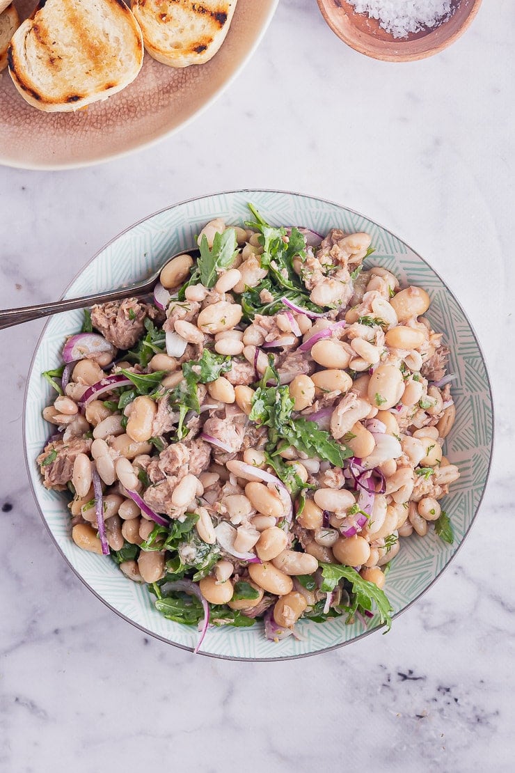 Overhead shot of healthy tuna salad with a spoon and toasts on a marble background