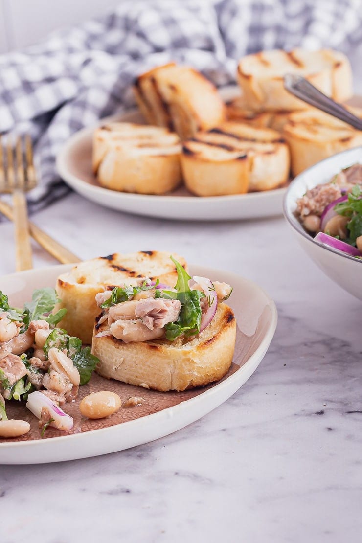 Garlic toasts with canned tuna salad on a pink plate on a marble surface