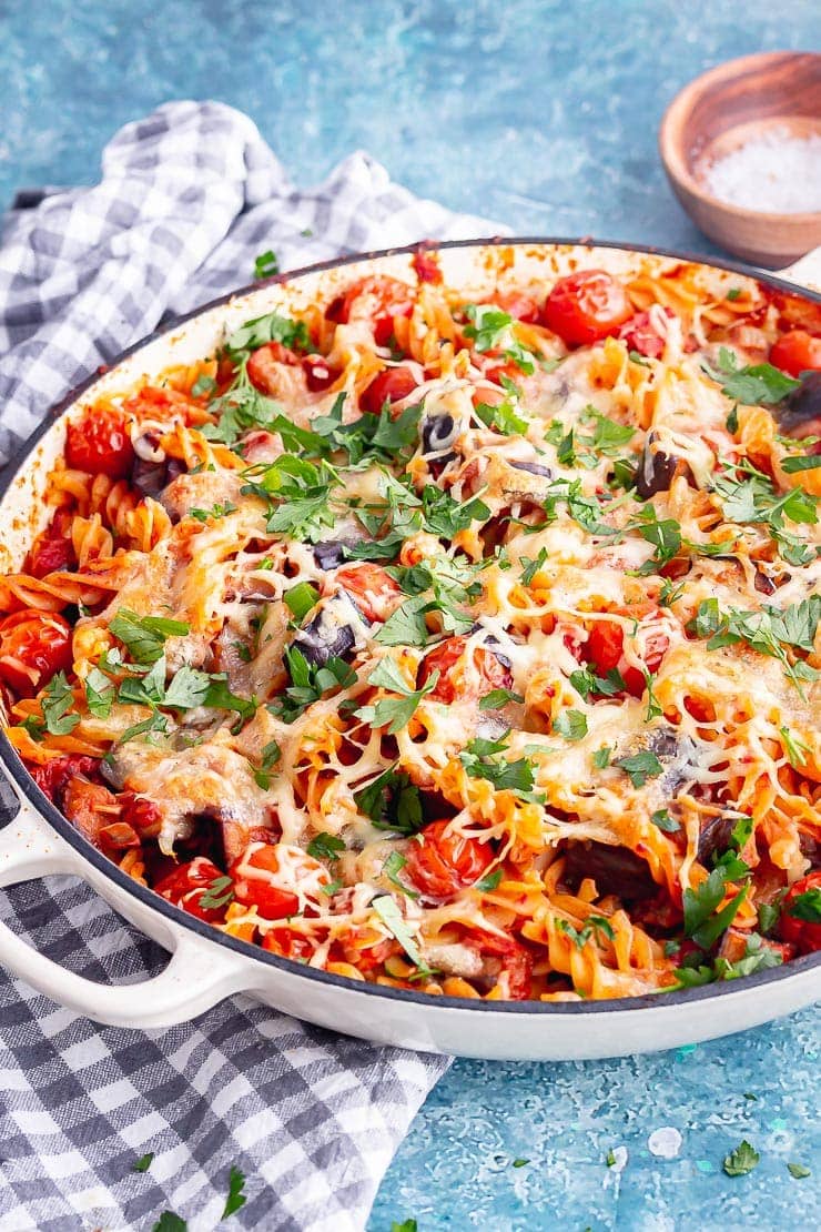 White baking dish of tomato and aubergine pasta on a blue surface