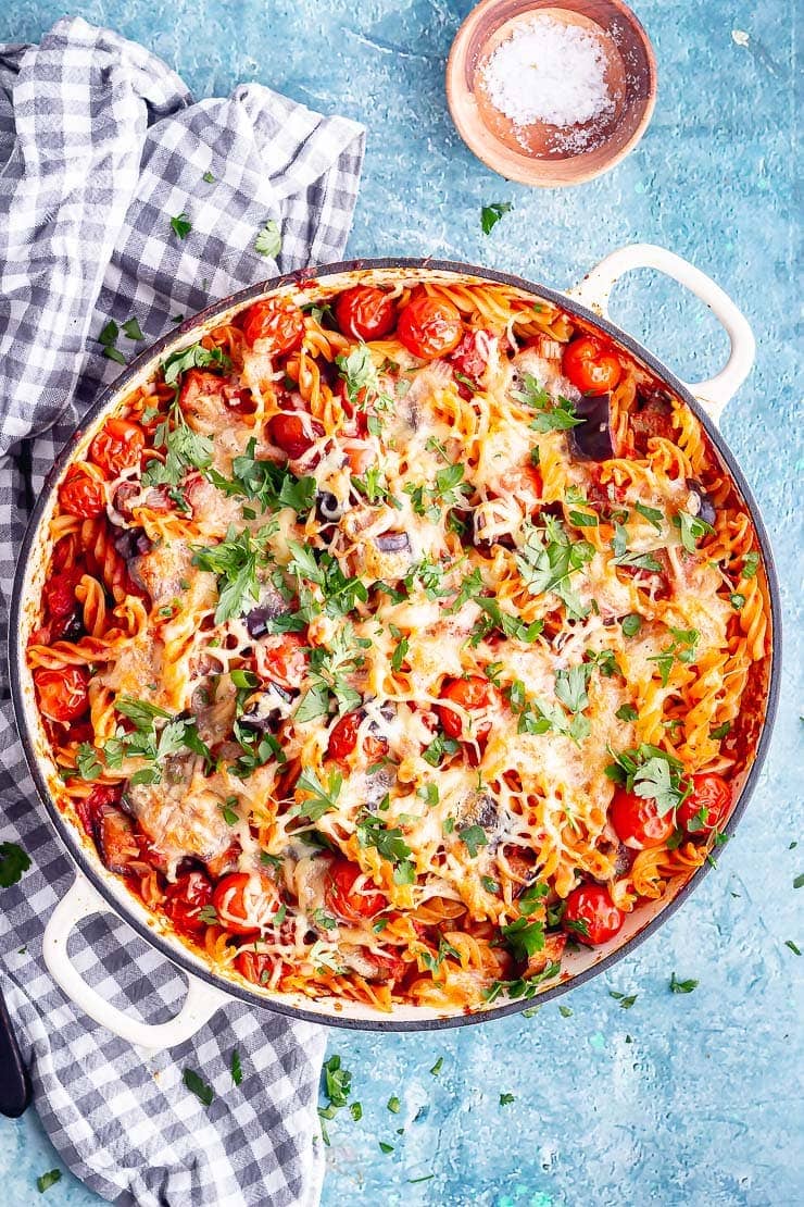 Overhead shot of aubergine pasta bake in a white dish on a blue background