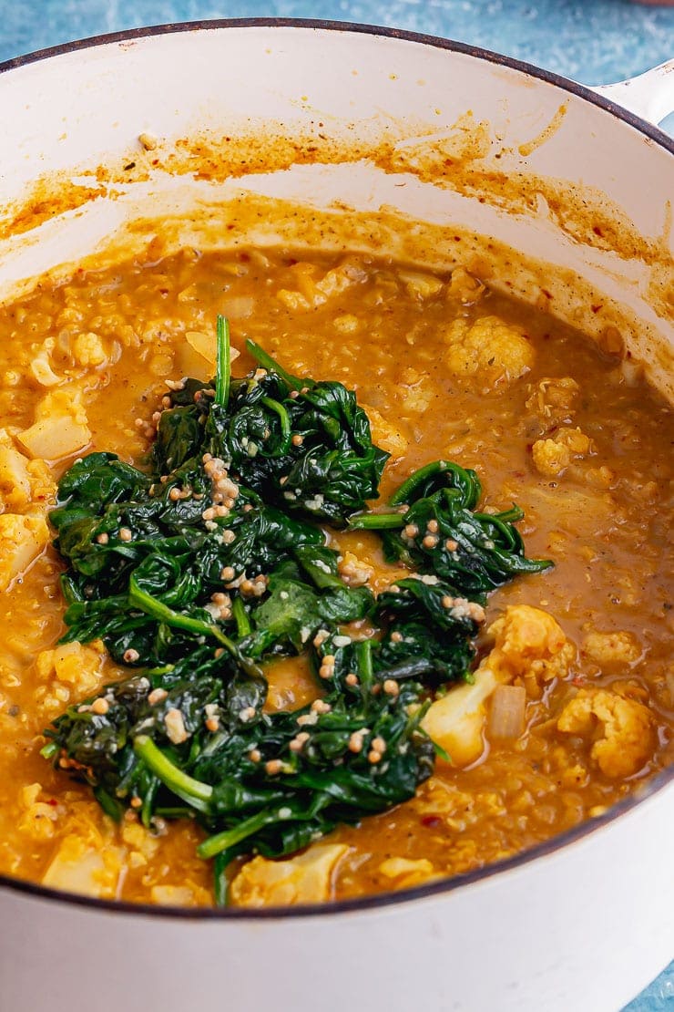 White pot of cauliflower lentil curry topped with spinach