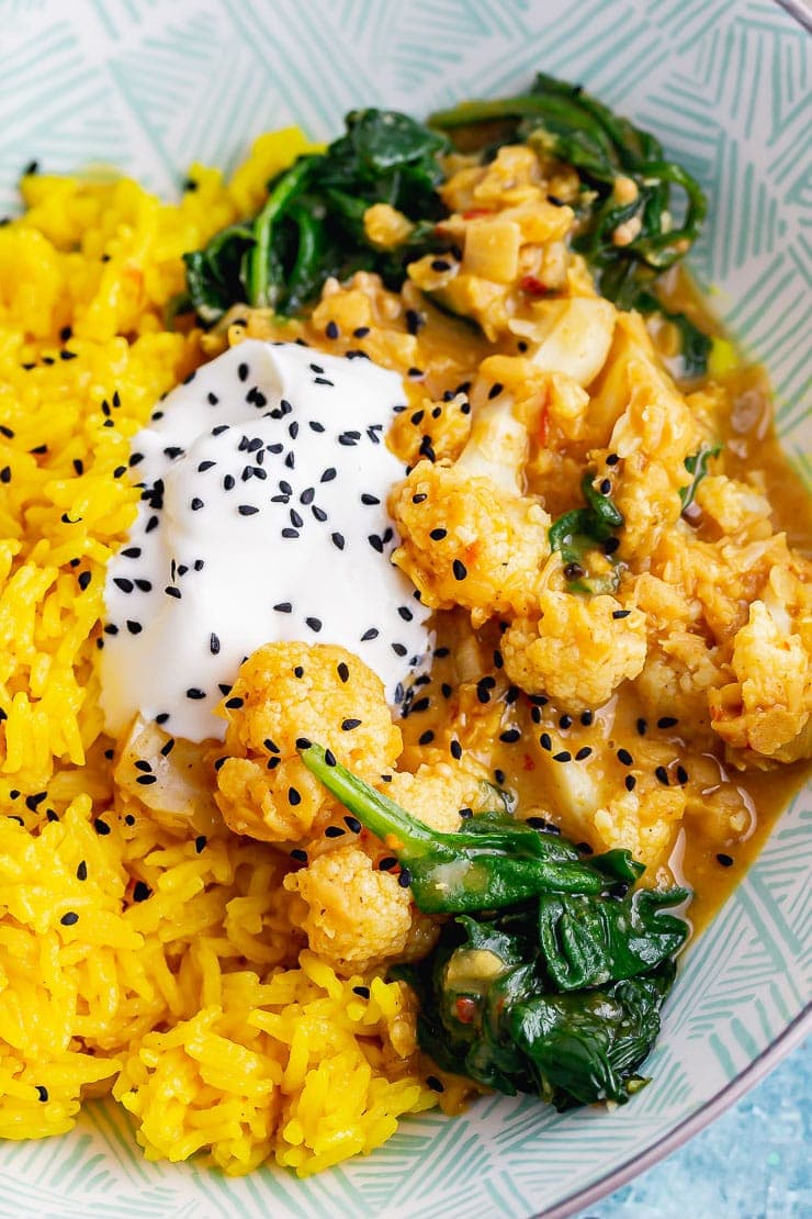 Close up of rice with yellow cauliflower curry topped with yoghurt