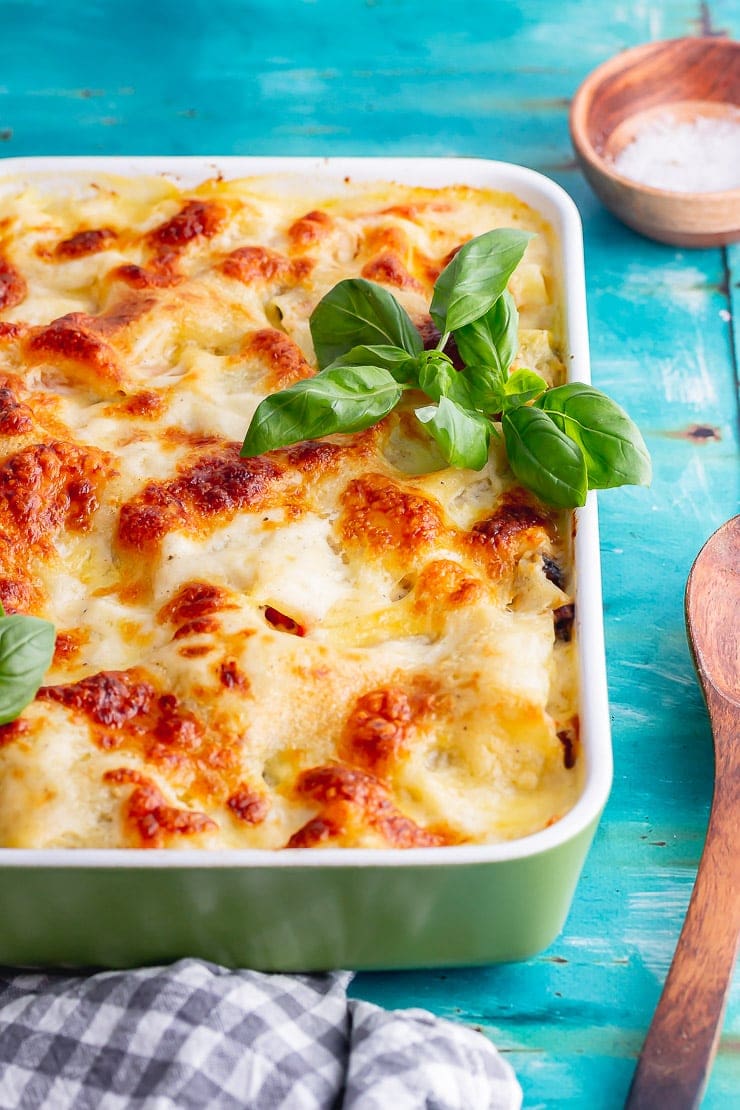 Veg lasagne on a blue surface with a wooden spoon