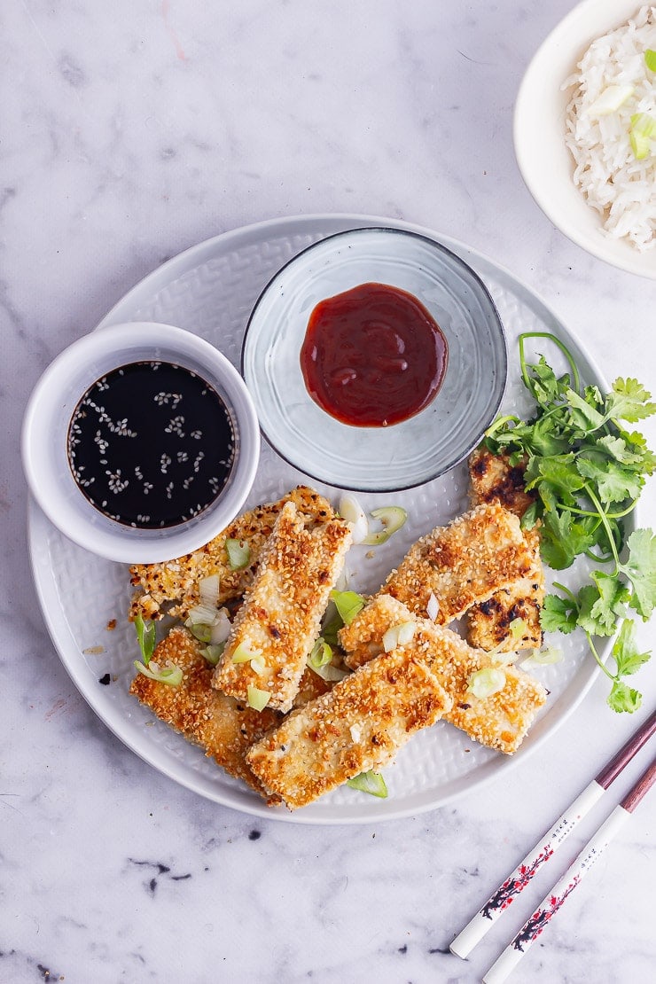 Grey plate of crispy fried tofu with sauce and herbs on a marble surface