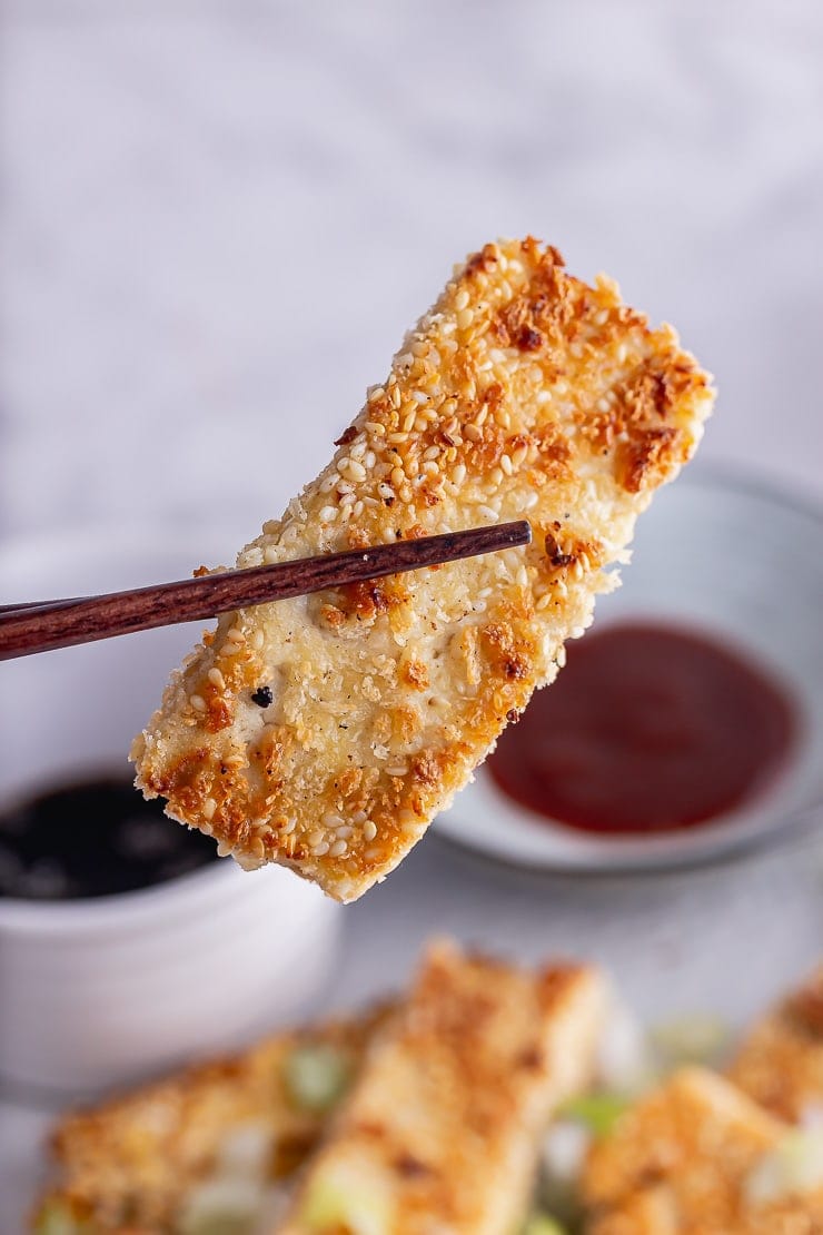 Chopsticks holding crispy tofu with sesame coating