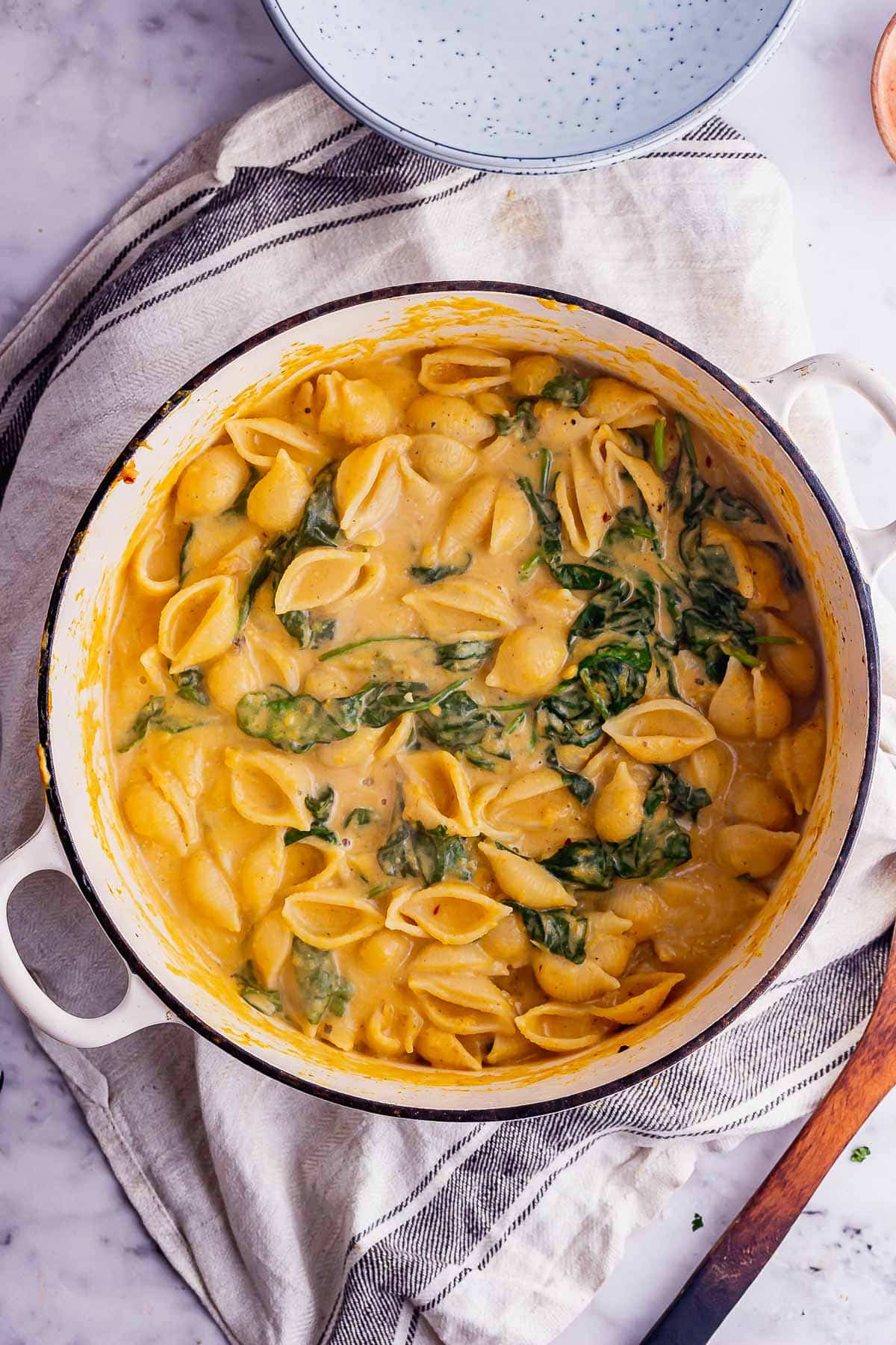 Overhead shot of a white pot of butternut pasta with spinach on a cream cloth
