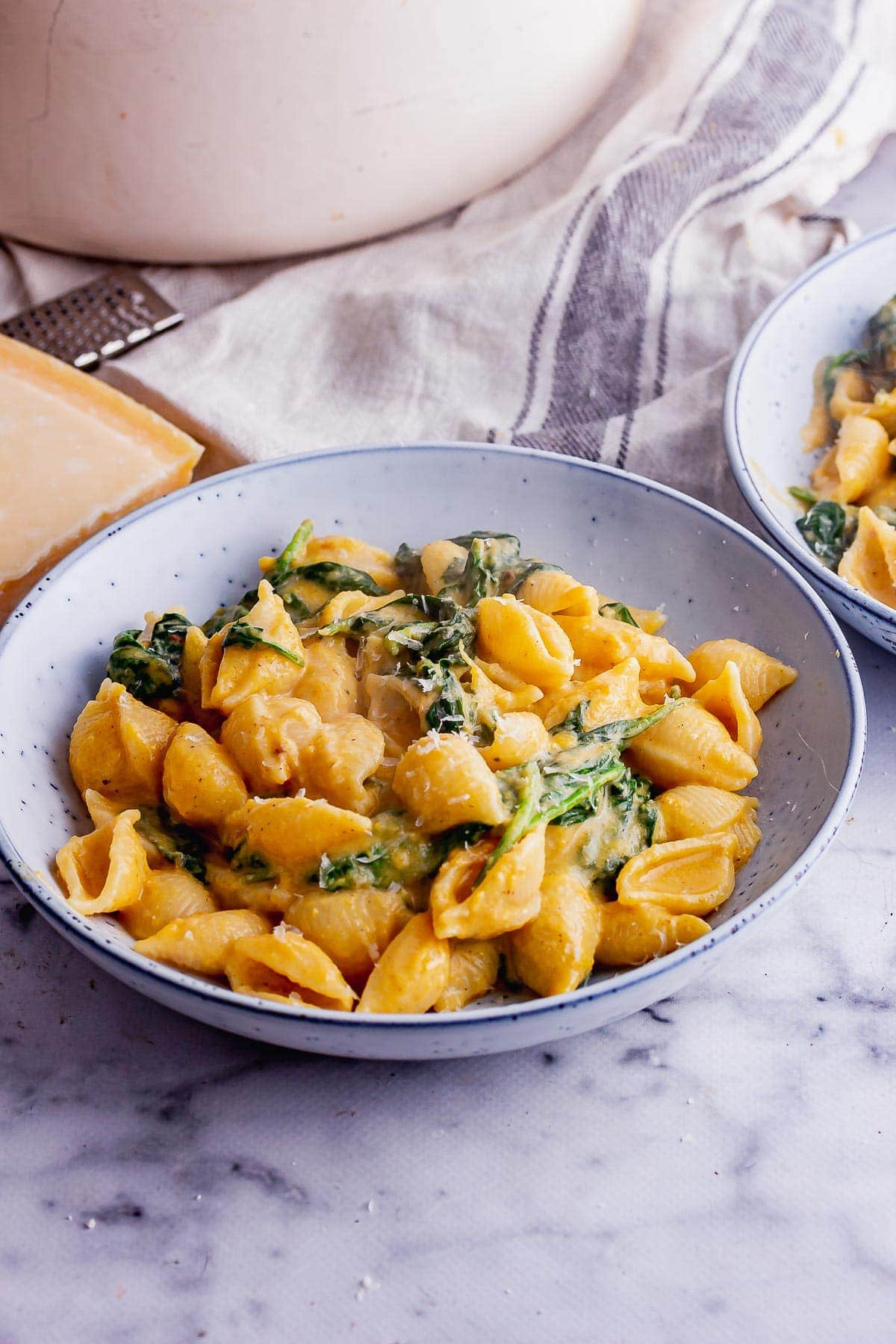 Blue bowl of butternut squash pasta sauce with spinach on marble background
