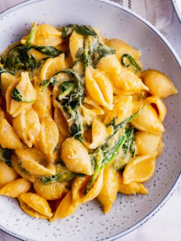 Overhead shot of butternut squash pasta sauce with spinach in a blue bowl