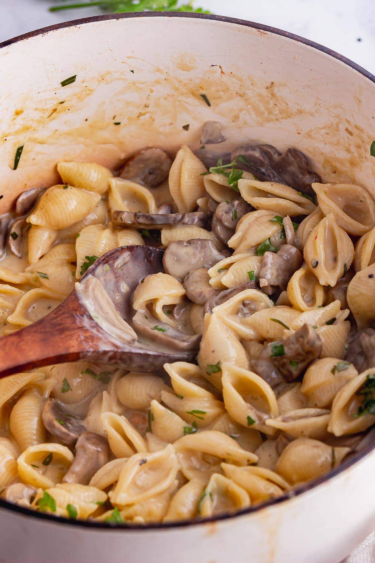 Wooden spoon in white pot of creamy mushrooms and pasta 