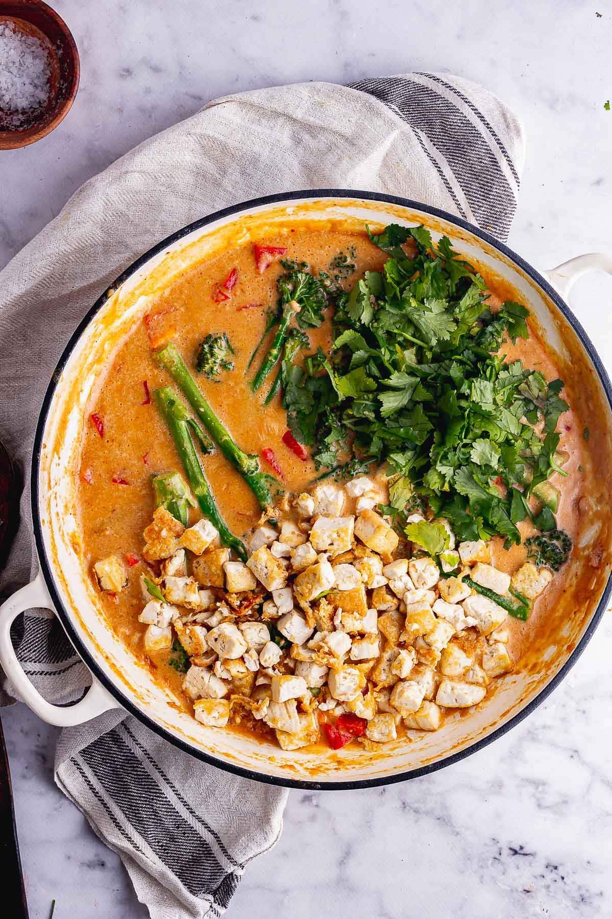 Overhead shot of peanut curry with broccoli and tofu on a marble background
