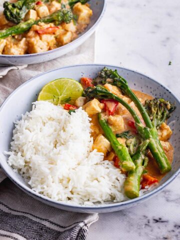 Blue bowl of veggie curry with peanut sauce and rice