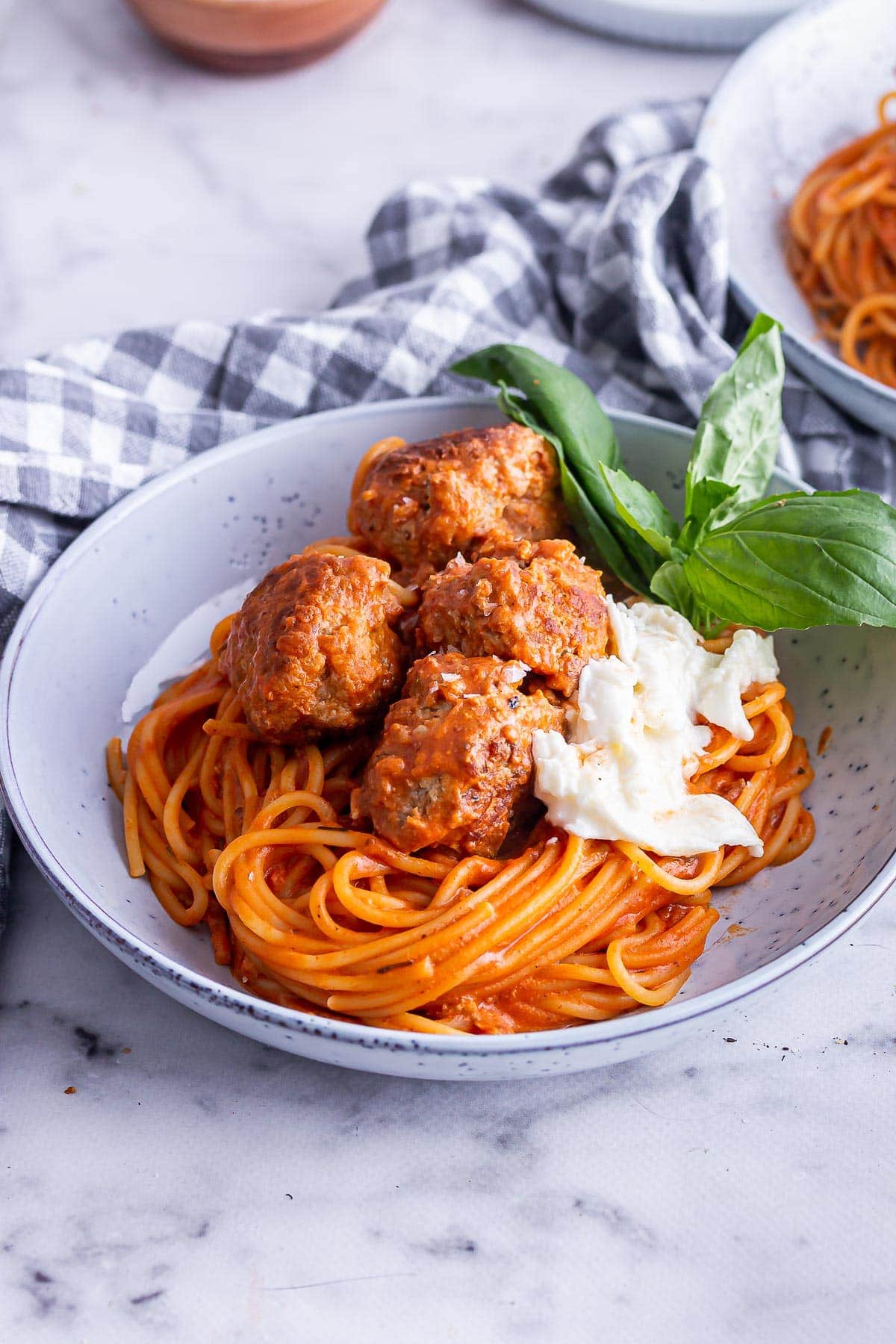 Blue bowl of spaghetti and meatballs with mozzarella and basil on a marble background