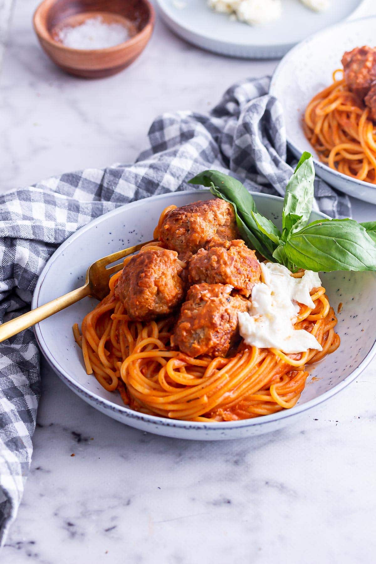 Blue bowl of meatballs and spaghetti with a gold fork