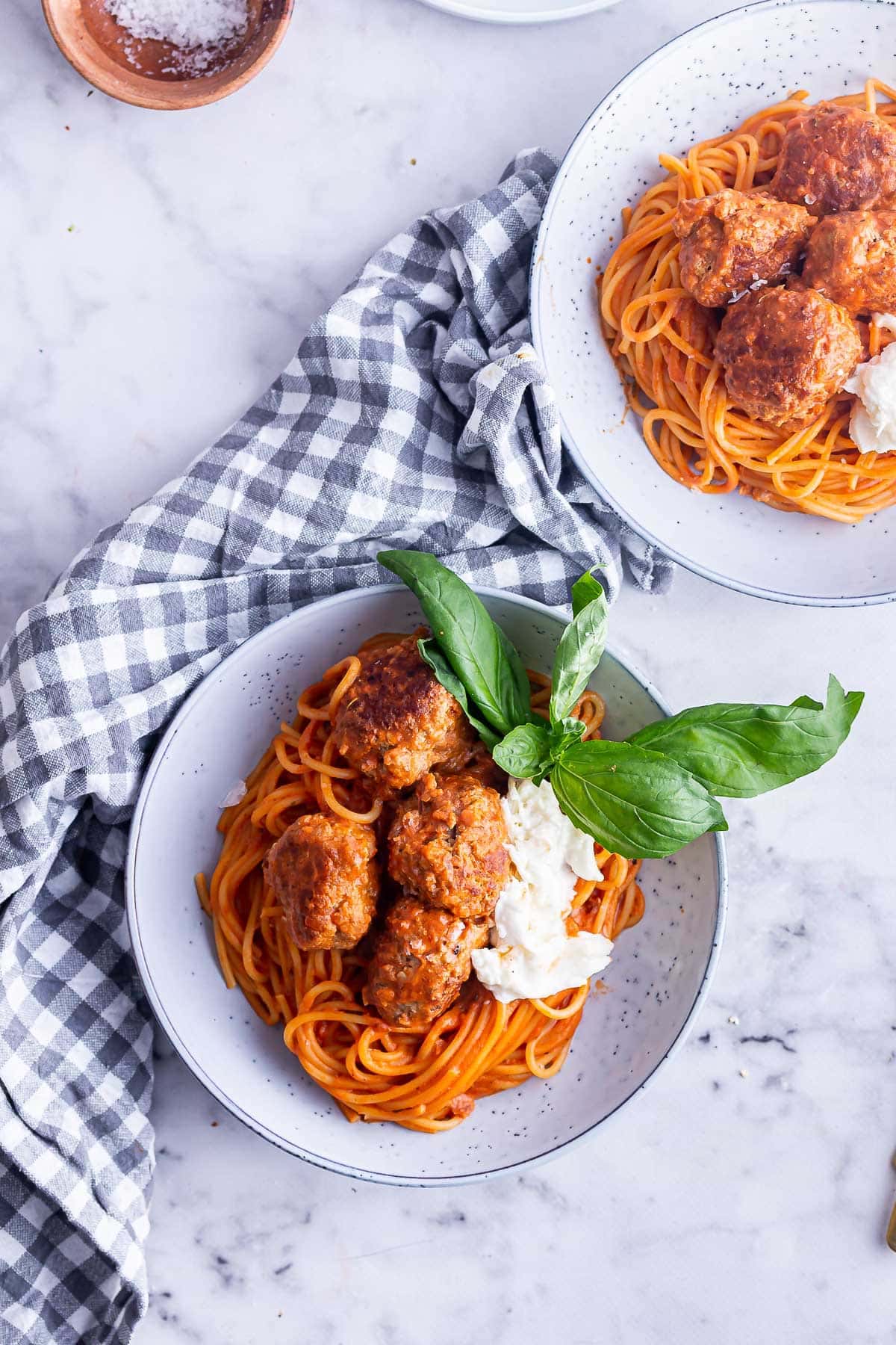 Overhead shot of two bowls of spaghetti meatballs with basil on a marble surface