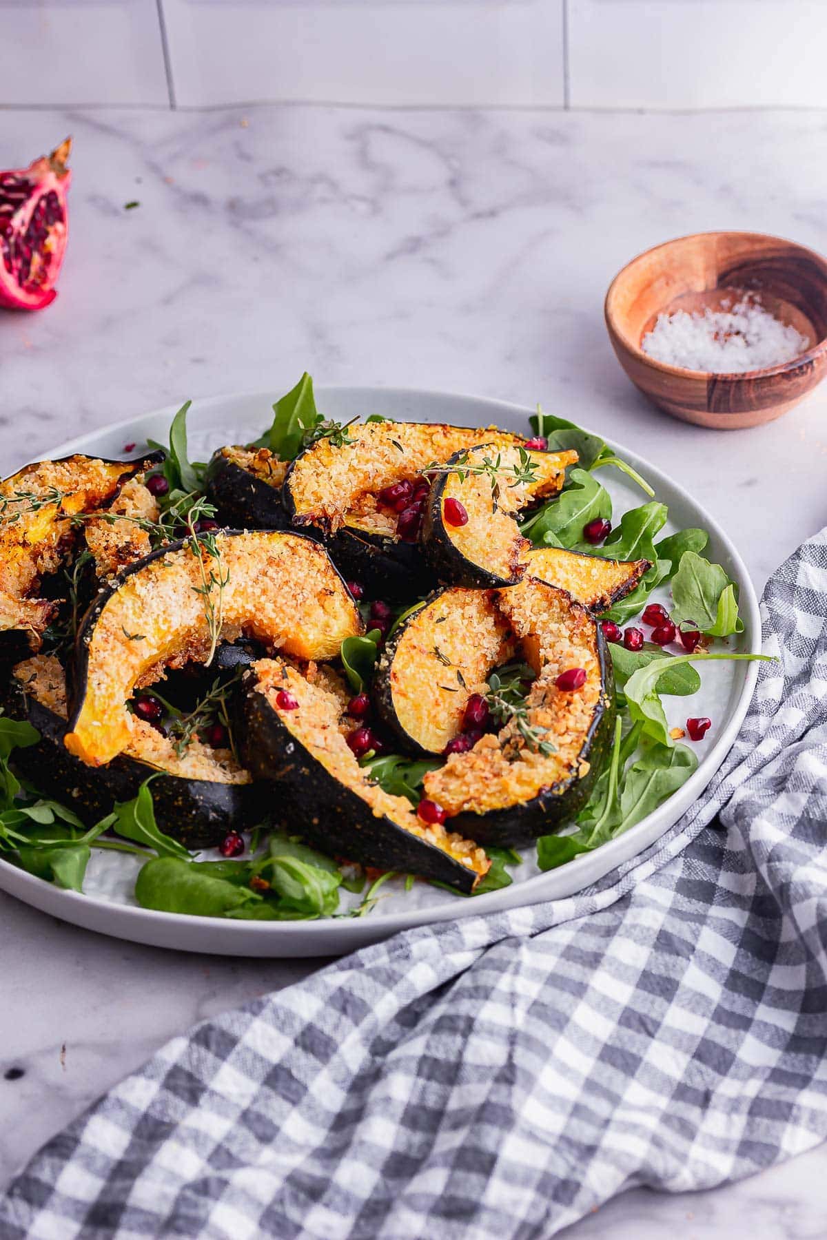 Grey plate of parmesan crusted squash on a bed of lettuce with a checked cloth