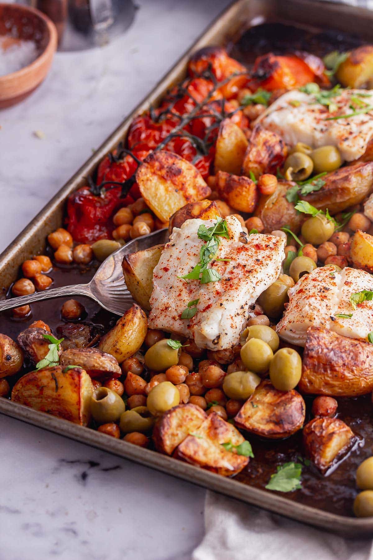 Sheet pan of cod and vegetables with a spoon