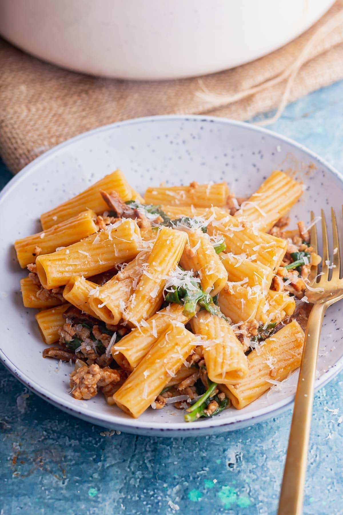 Blue bowl of pork rigatoni with a gold fork