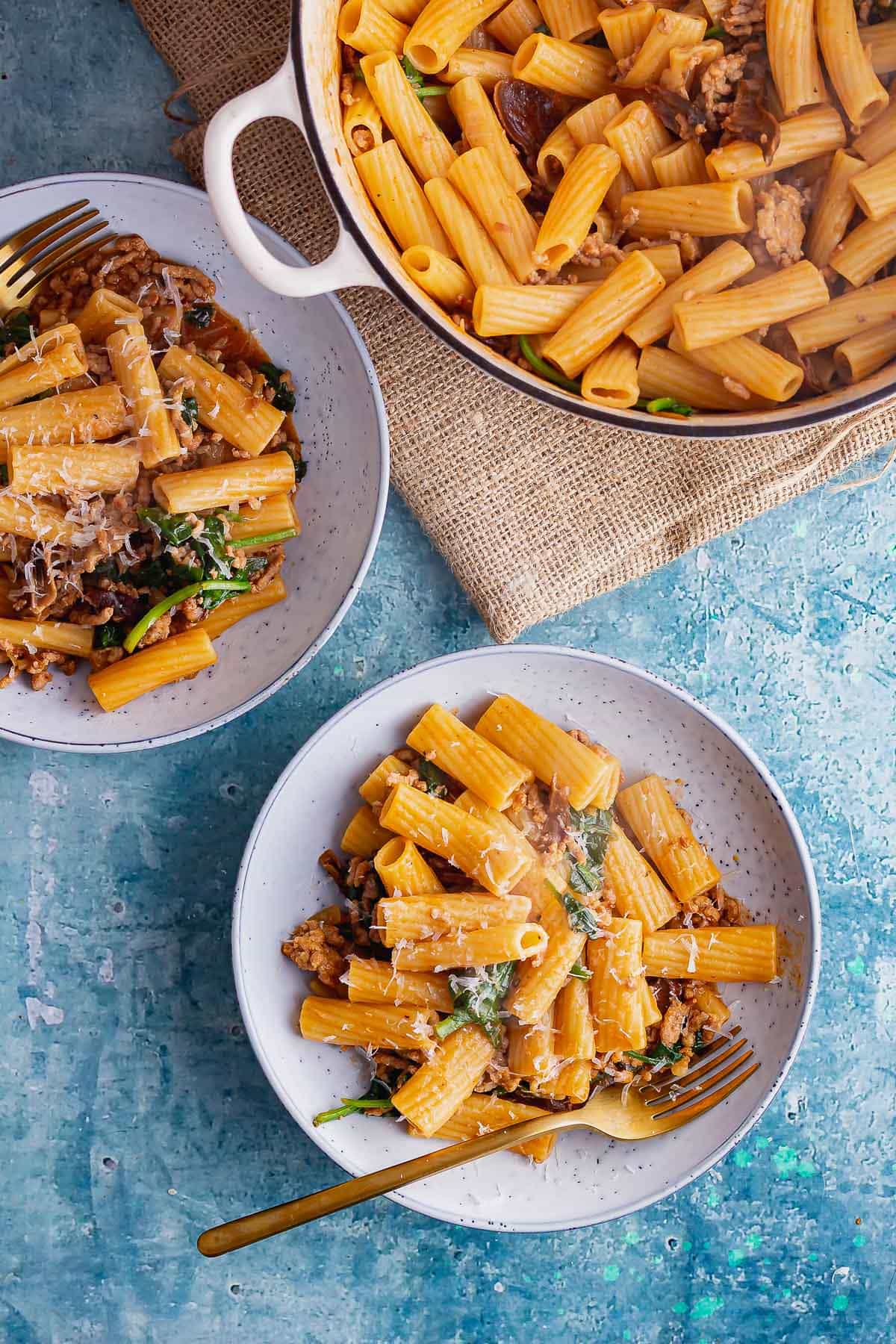 Overhead shot of pork mince pasta on a blue background with a gold fork