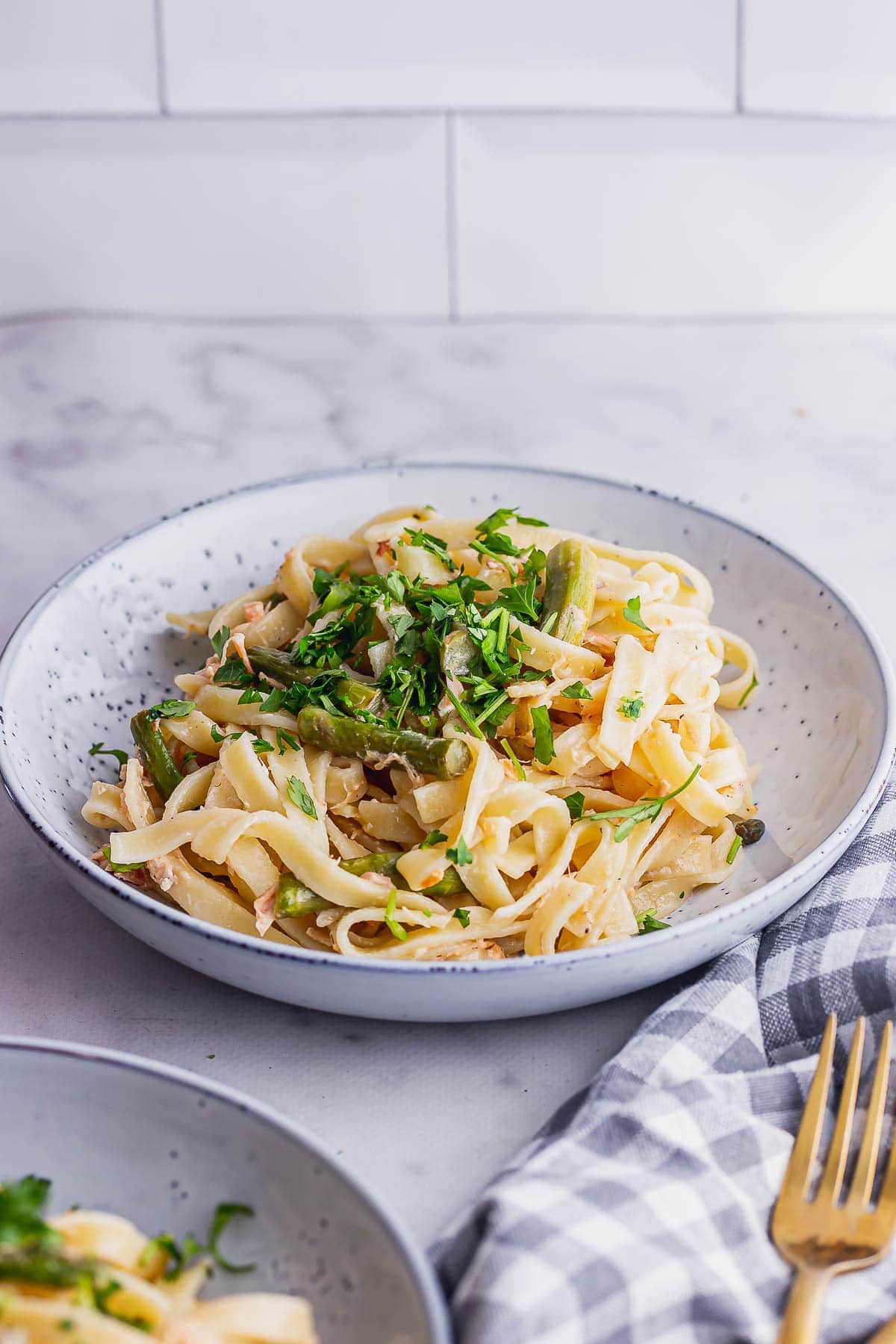 Blue bowl of salmon pasta in front of a white brick wall