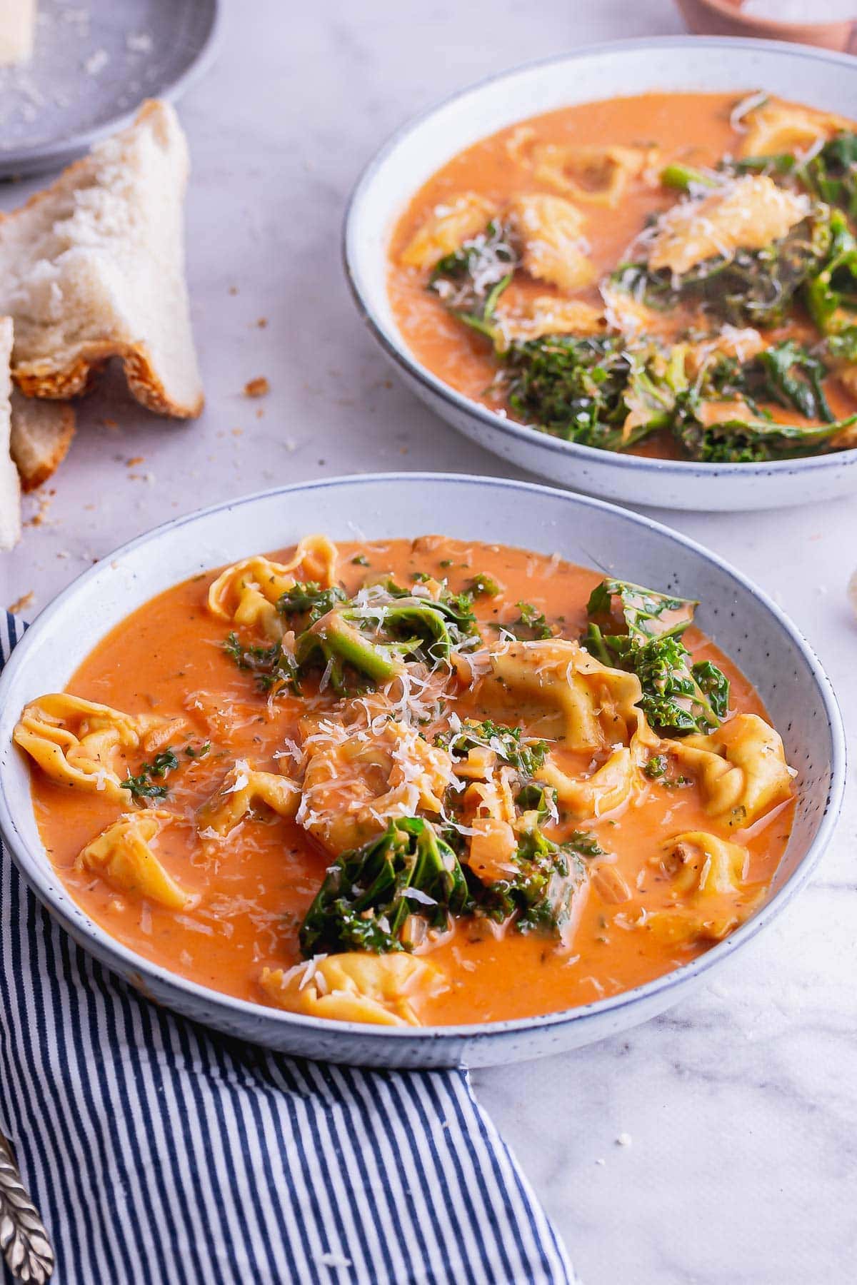 Blue bowl of creamy tortellini soup on a marble background