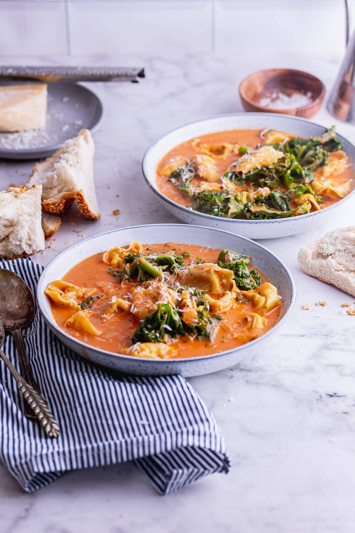 Side shot of blue bowls of creamy pasta soup with kale and a striped cloth