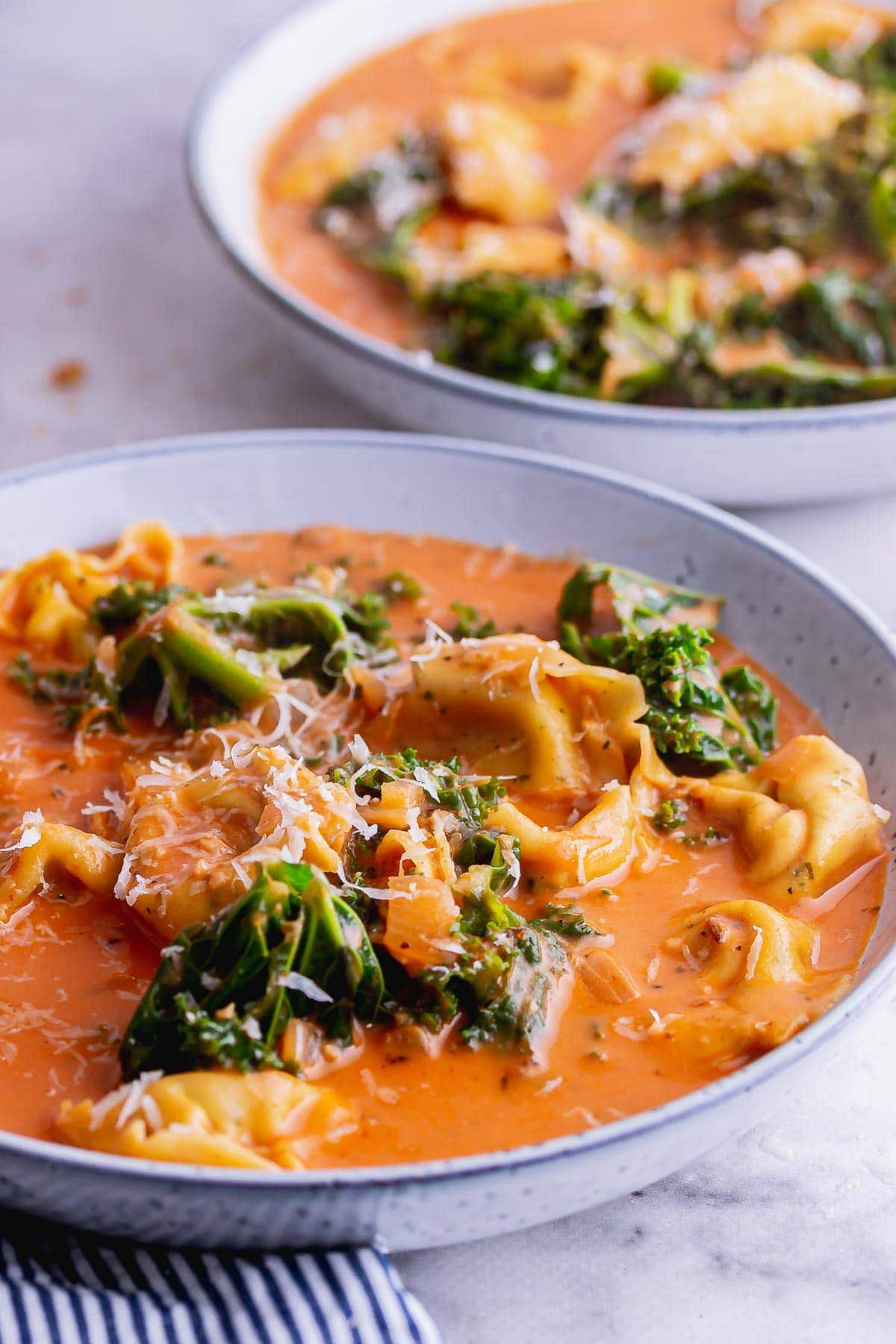 Close up of cheesy pasta tomato soup with kale in a blue bowl