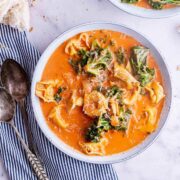 Overhead shot of creamy tomato and tortellini soup with a striped cloth