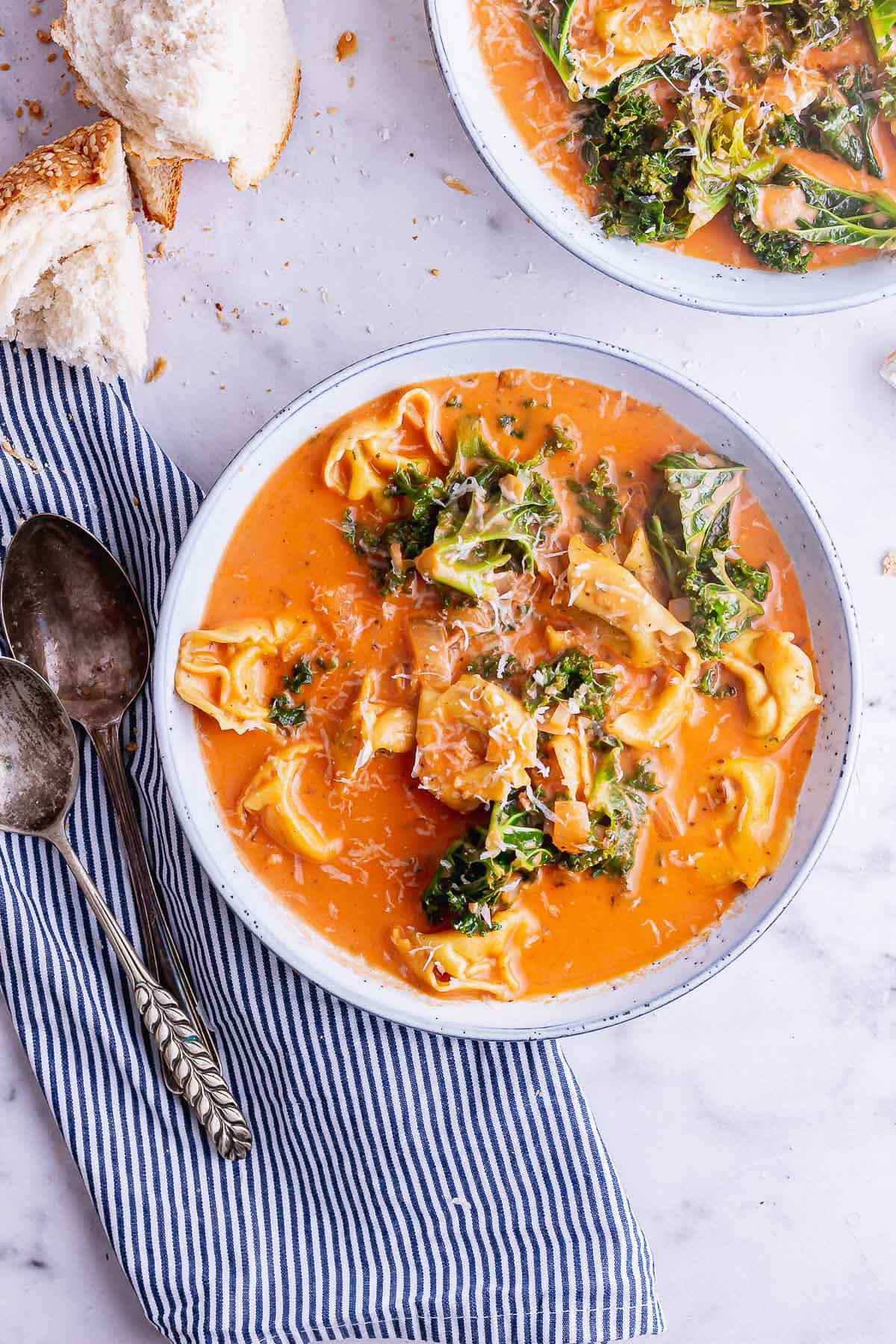 Overhead shot of creamy tomato and tortellini soup with a striped cloth