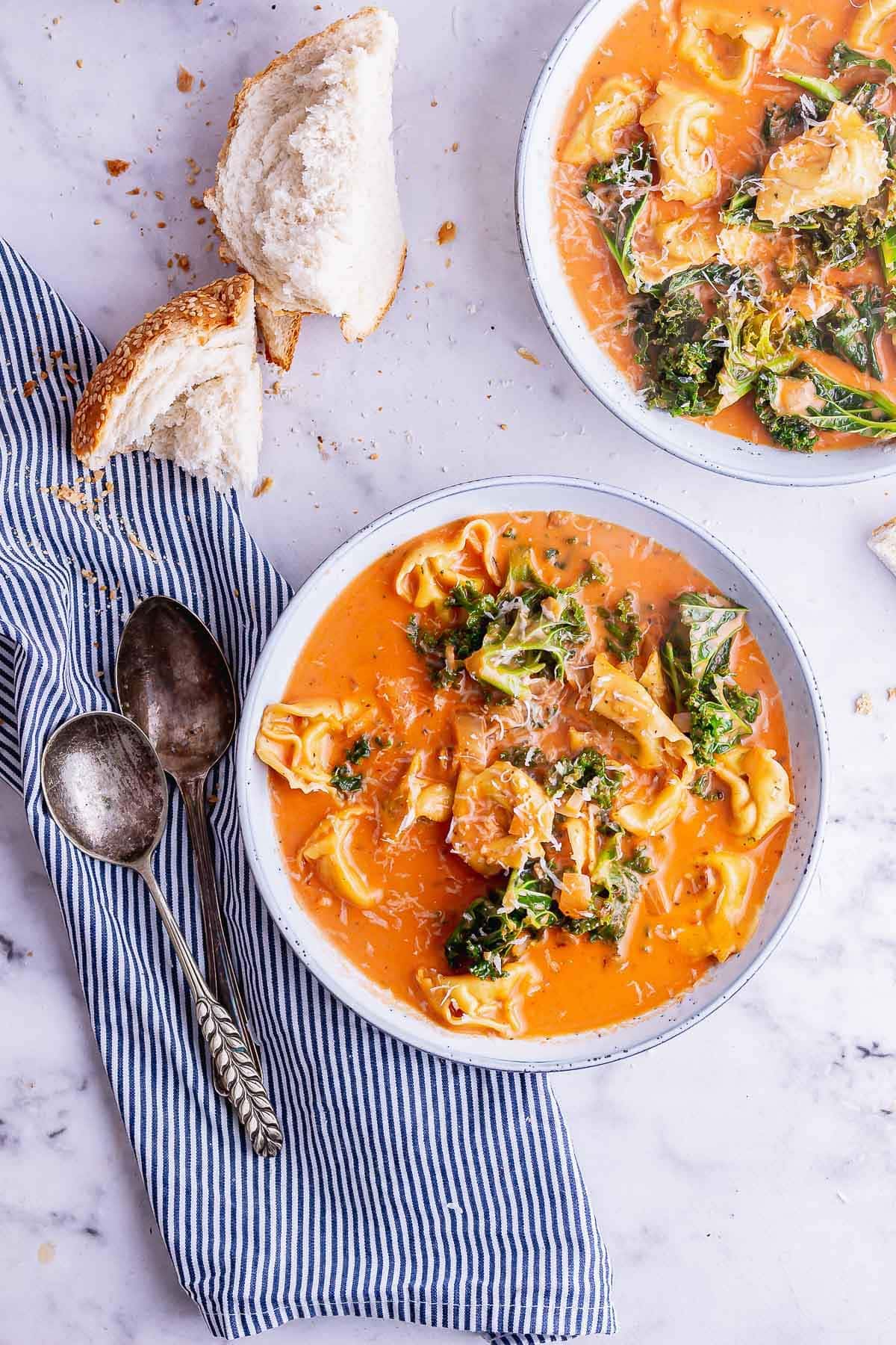 Two bowls of creamy tortellini soup with a striped napkin on a marble background